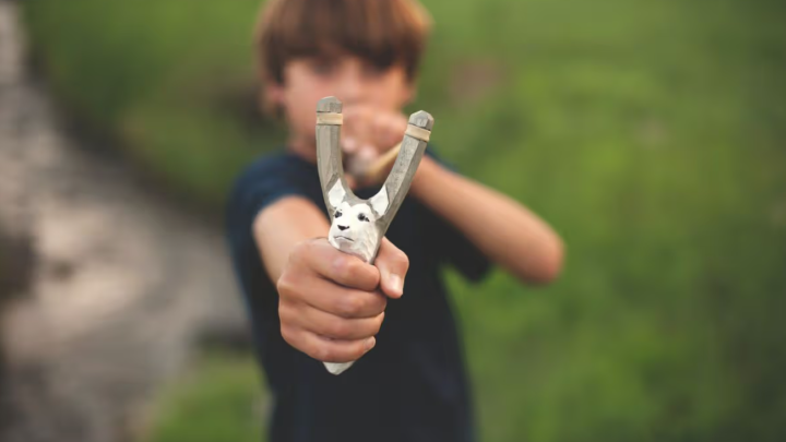 child practicing slingshot shooting outdoors with focus and safety